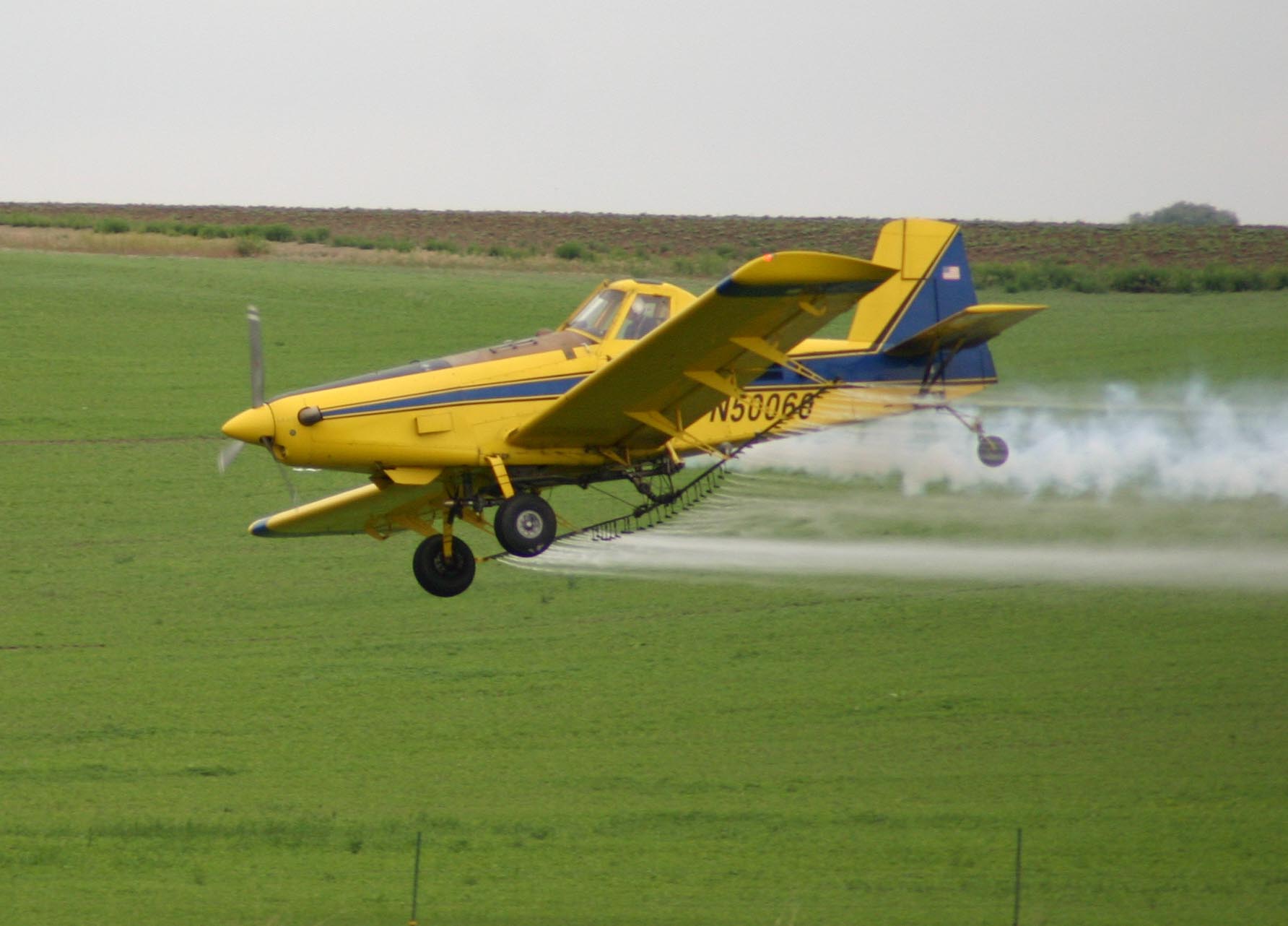 Yellow Air Tractor pulling up from a green field with spray trailing behind it